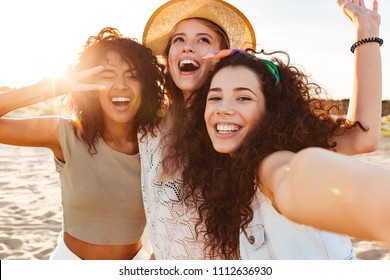 Three cheerful girls friends in summer clothes taking a selfie at the beach
