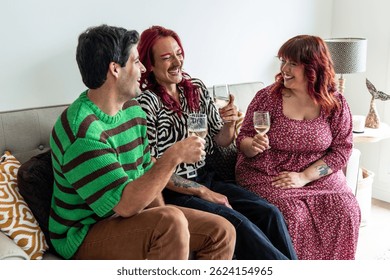 Three cheerful non-binary friends of diverse body types and styles smiling and raising glasses of white wine on a cozy sofa, celebrating body positivity and LGBTQ+ pride