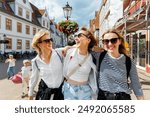 Three cheerful young adult women friend with kids walk street old european german town city street enjoy having fun laughing sunny day together. Female persons friendship celebration party weekend