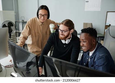 Three Cheerful Young Intercultural Diversity Programmers Decoding Data On Computer Screen At Working Meeting In Bureau