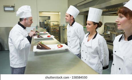 Three chefs presenting their plates to the head chef in a kitchen - Powered by Shutterstock