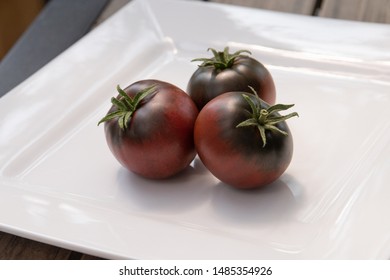 Three Cherokee Purple Tomatoes On A White Plate. 