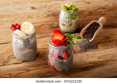 Three Chia Pudding In Glass Jar Stawberry Banana Kiwi On Wooden Plank