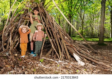 Three children boys and a girl with pile of brushwood in the forest build hut of branches in summer school