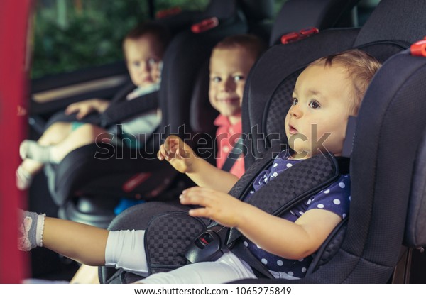 Three children in car safety seat -\
family, transport, safety, road trip and people\
concept