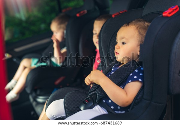Three children in car safety seat -\
family, transport, safety, road trip and people\
concept