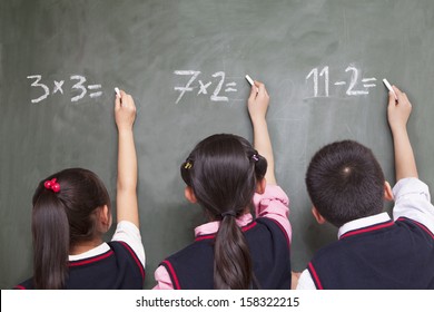 Three Children Doing Math Equations On Blackboard