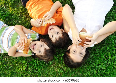 Three children laying on green grass on ground and eating sandwiches and smiling, healthy food, good friendship and love and happiness without limit :) - Powered by Shutterstock