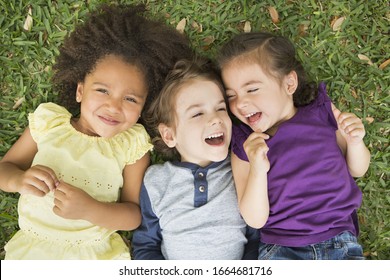 Three children lying on their backs on the grass, looking up and laughing. - Shutterstock ID 1664681716