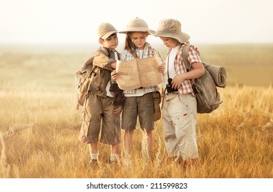 Three children with maps and travel backpacks on steppe valleys in summer at sunset - Powered by Shutterstock