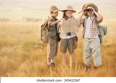 Three children with maps and travel backpacks on steppe valleys in summer at sunset