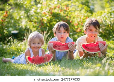 Three children, siblings and pet dog, eating watermelon in garden, summertime - Powered by Shutterstock