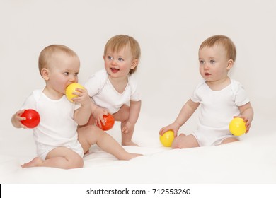 Three Children Are Sitting In White T-shirts On A White Background. Triplets Play On A White Background