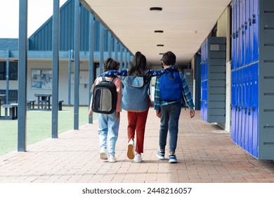 Three children are walking down a school corridor, arms over each other's shoulders. The biracial boy and girls, with backpacks, share a moment of friendship amidst the lockers and open space. - Powered by Shutterstock