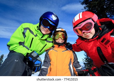 Three Children Wearing Colorful Ski Goggles And Winter Jackets Outdoors.