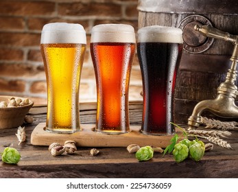 Three chilled glasses of different beer and beer barrel on wooden table closeup.  - Powered by Shutterstock