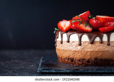 Three chocolates cake with chocolate drips on a black background. Layered cake with milk, black and white chocolate souffle decorated with strawberries on top. Confectionery background with copy space - Shutterstock ID 1921040348