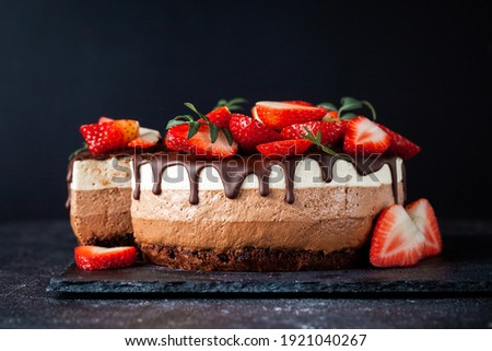 Three chocolates cake with chocolate drips on a black background. Layered cake with milk, black and white chocolate souffle decorated with strawberries on top. Confectionery background with copy space