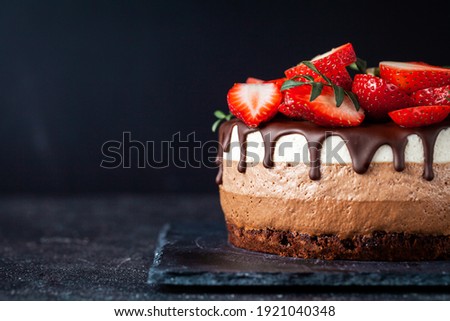 Three chocolates cake with chocolate drips on a black background. Layered cake with milk, black and white chocolate souffle decorated with strawberries on top. Confectionery background with copy space