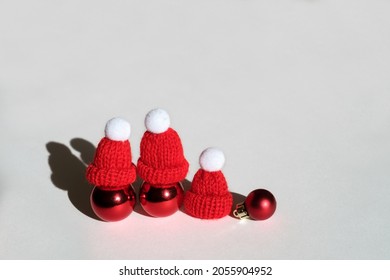 Three Christmas Balls In Red Knitted Hats On A White Background. A Warm Winter Hat So As Not To Get Sick In The Cold Winter. The Concept Of Christmas And New Year. Light And Deep Shadow. Xmas