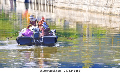 Three cleaner workers in a boat are cleaning and collecting trash in a moat at Bangkok, Thailand - Powered by Shutterstock