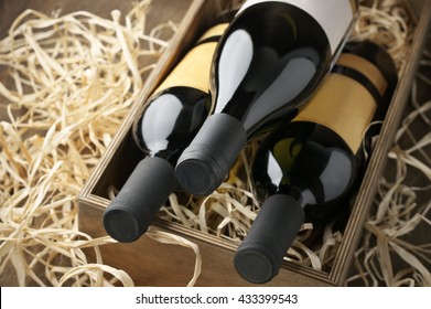 Three closed wine bottles lying on straw in vintage wooden box.