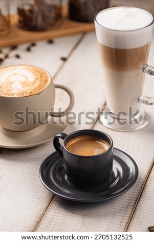 Three coffee drinks including espresso latte and cappuccino served on a wooden table with beans around