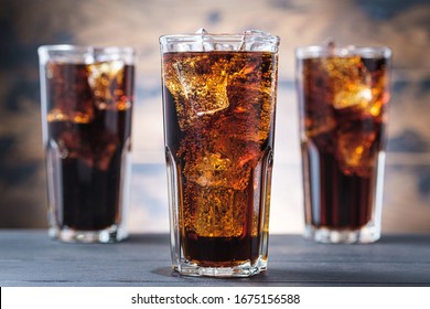 Three cola glass with ice cubes and bubbles. Cold sweet drink on wooden background