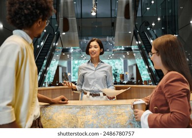 Three colleagues, chat and laugh while standing in an office lobby.