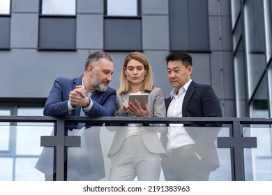 Three Colleagues, Diverse Business Group, Business People Outside Office Building Talking And Discussing Work Process, Looking At Tablet Computer Thoughtfully