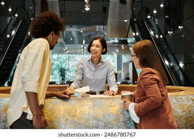 Three colleagues, stand near a reception desk, smiling and talking. - Powered by Shutterstock