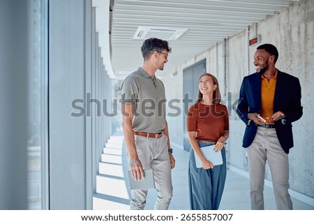 Three colleagues are walking through a modern office building, discussing work and collaborating on a project