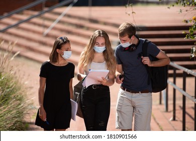 Three College Students Wearing Face Masks Chatting While Walking Outdoors In The Campus During The Coronavirus Pandemic.