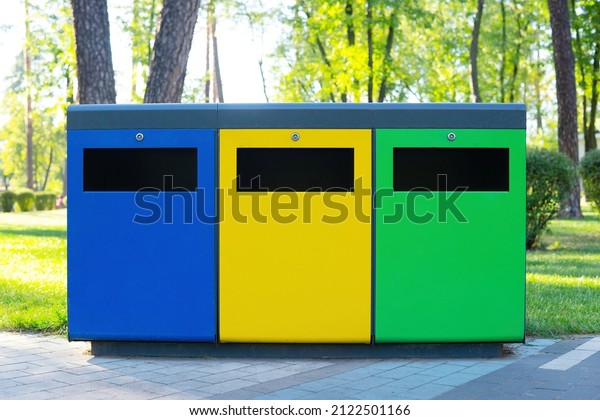 Three colored garbage bins\
for waste collection and sorting in the public park. Waste\
recycling concept.