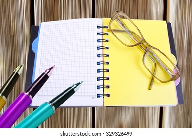 three colored pen with a notebook on a wooden background
