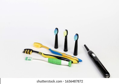 Three Colored Toothbrushes And A Black Modern Electric Toothbrush With Three Nozzles On A White Background For The Whole Family.Top Angle View