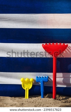 Three colorful childrens beach toys in a sand in front of a wind screen