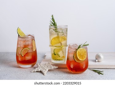 Three Colorful Christmas Cocktails In Glasses On White Table. Assortment Of Fresh Holiday Drinks. Strawberry Mojito, Orange Punch Cocktail, Tropical Mule.