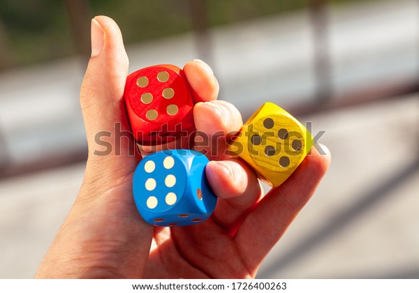 Three colorful game dice held in hand showing\
number six, three sixes. Holding 3 colored dice between fingers,\
lucky throw, luck in gambling, winning abstract concept, success,\
good odds symbolic