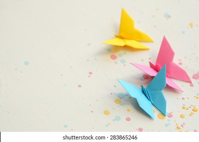 Three colorful origami butterflies on white wooden background splashed with paint