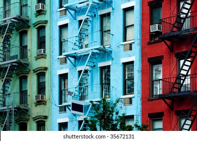 Three colorful, red, blue and green, apartment buildings facades with emergency escapes. Typical New York City, Boston  or Chicago rental complexes with fire escape stairs next to the windows.