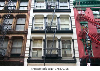 Three colorful, red, brown and white, apartment buildings facades with emergency escapes. Typical New York City rental complexes with fire escape stairs next to the windows.