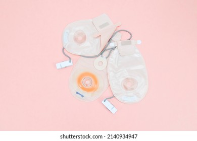 Three colostomy bags with medical clips lie on a pale pink background, flat lay close-up. Colon cancer concept, surgery and operations planning.
