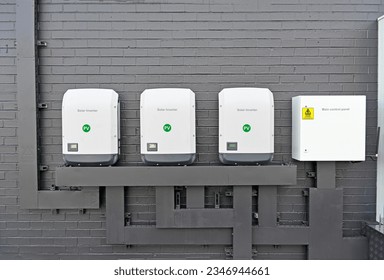 Three commercial size solar inverters and a control panel on a brick wall