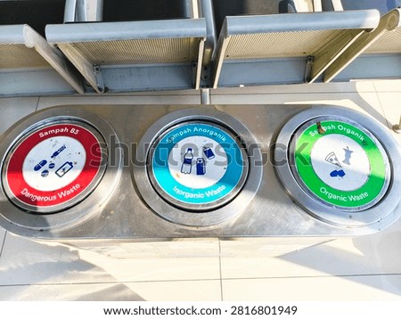 Three compartment waste sorting bin stainless steel, color coded lids for dangerous, inorganic, and organic trash separation in public station area.