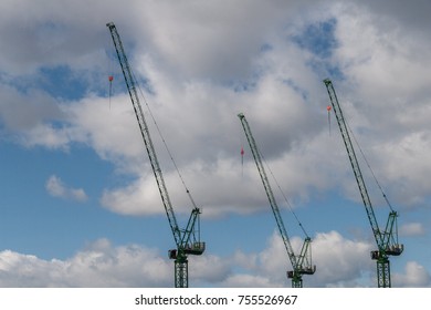 Three construction cranes towering the blue cloudy sky 