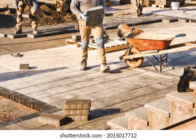 Three construction workers laying interlock driveway pavers and working on a landscaping construction site. Contractors working as team to design and construct large home landscape business project.