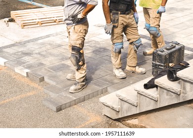 Three construction workers working on landscaping construction site, laying paving driveway stones slabs for quality garden patio stonework, home renovation project. Prospective view of man onsite job