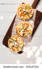 Three Cooked Delicious Mini Vegetarian Pizzas On A Long Wooden Board Standing On A White Painted Wooden Table Outdoors In Dappled Sunlight, Overhead View