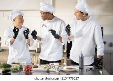 Three cooks with different nationalties tasting cooked meals, inventing new dishes for a menu. Caucasian chef with Latin and Asian cooks in uniform working together. Concept of teamwork and high